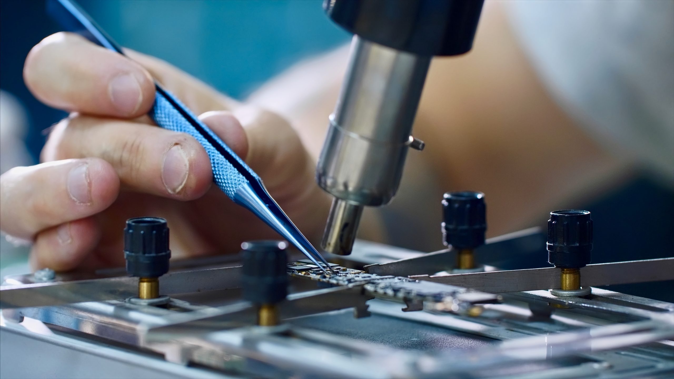 Electronics engineer repairing chip in workshop, hands closeup. Repairman heating chipset using soldering blow dryer and taking hot melting element forceps. Repair and maintenance service center.